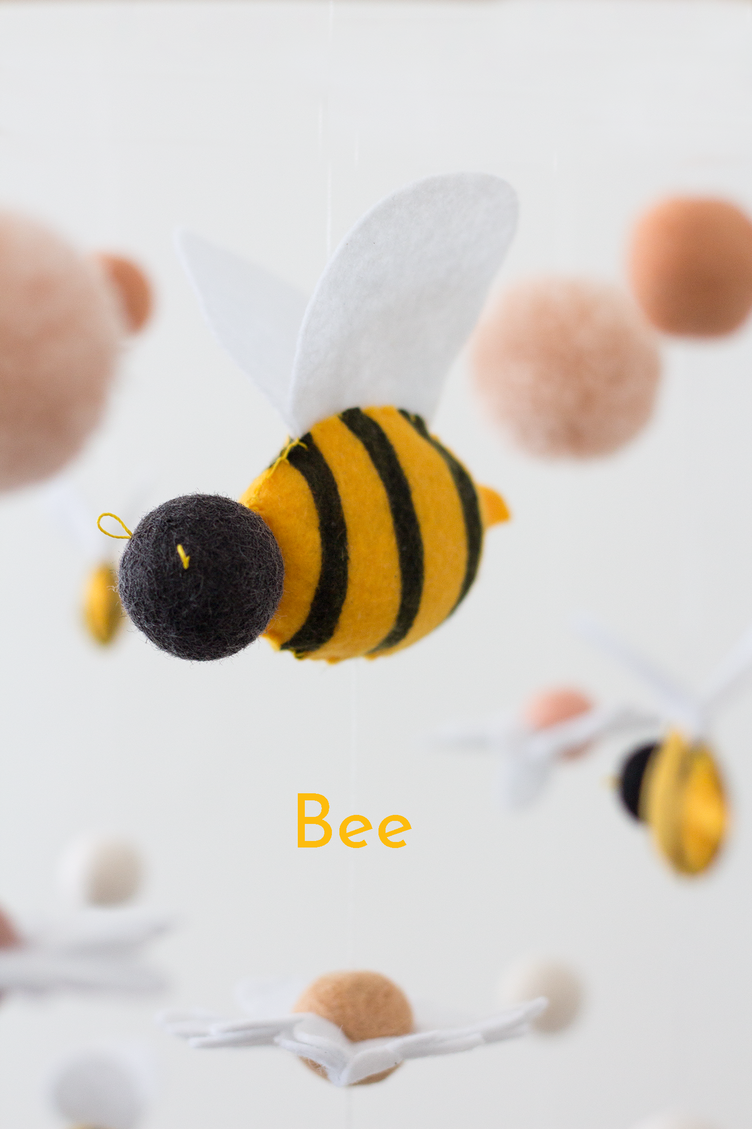 A felt bee ornament or decoration with yellow and black stripes, a black head, white wings shown against a soft white background