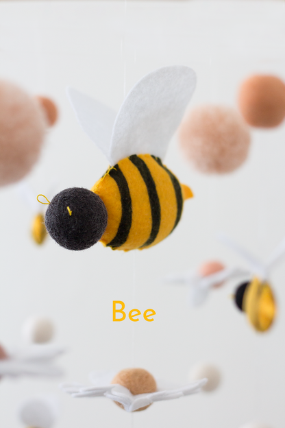 A felt bee ornament or decoration with yellow and black stripes, a black head, white wings shown against a soft white background